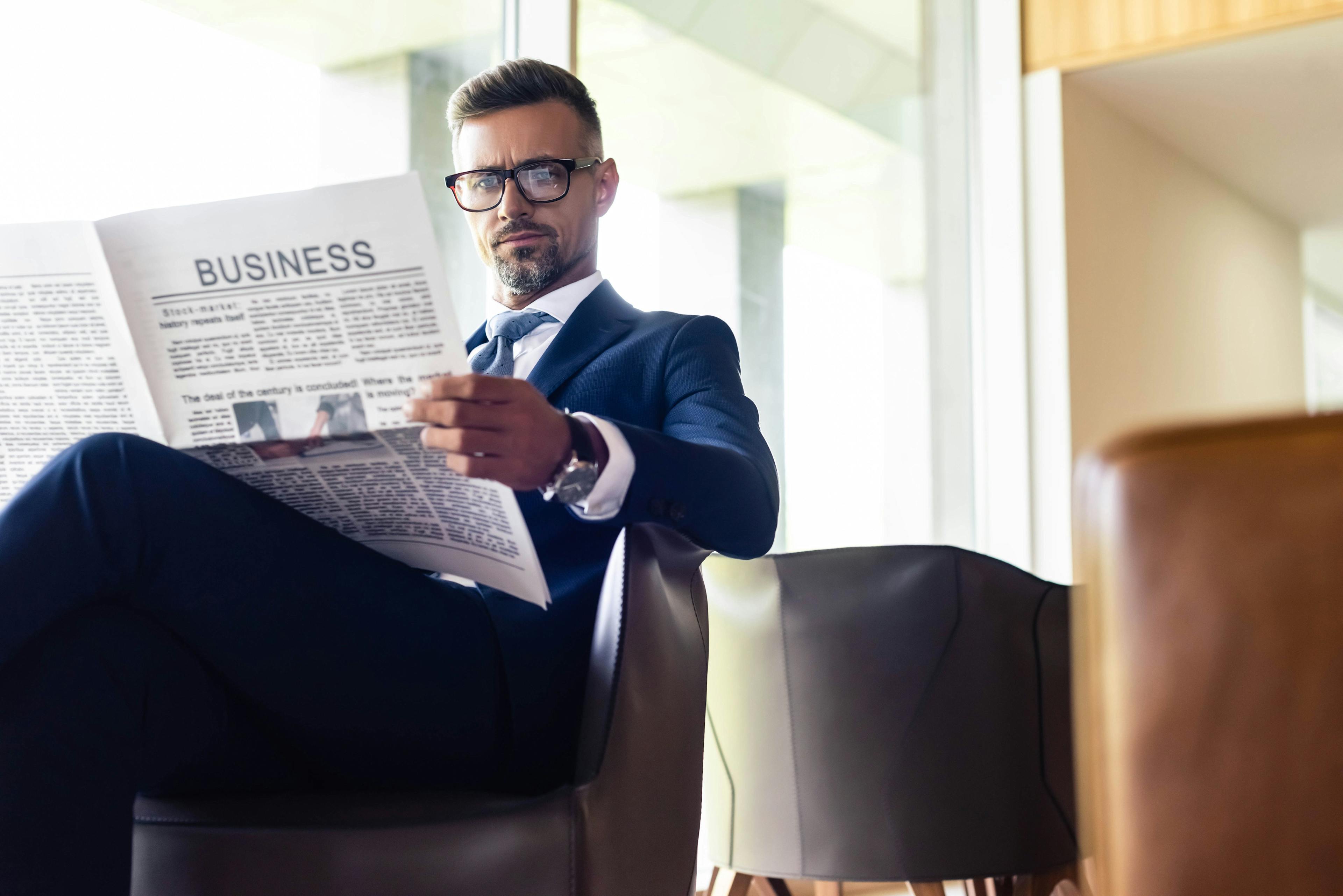 handsome businessman in suit and glasses reading newspaper business | Image Credit: © Lightfield Studios - stock.adobe.com.