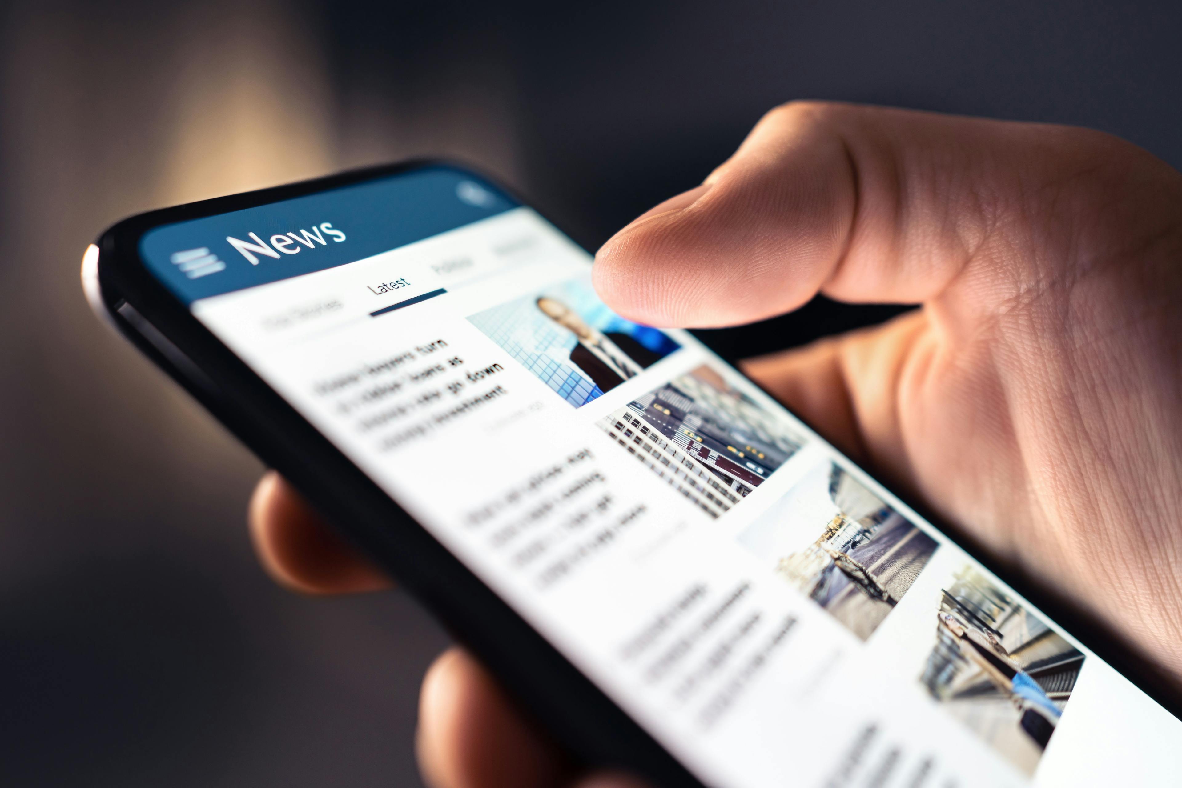 News feed in phone. Watching and reading latest online articles and headlines from smartphone newspaper mobile app. Daily digital information portal and publication. Media and press on internet. | Image Credit: © terovesalainen - stock.adobe.com.