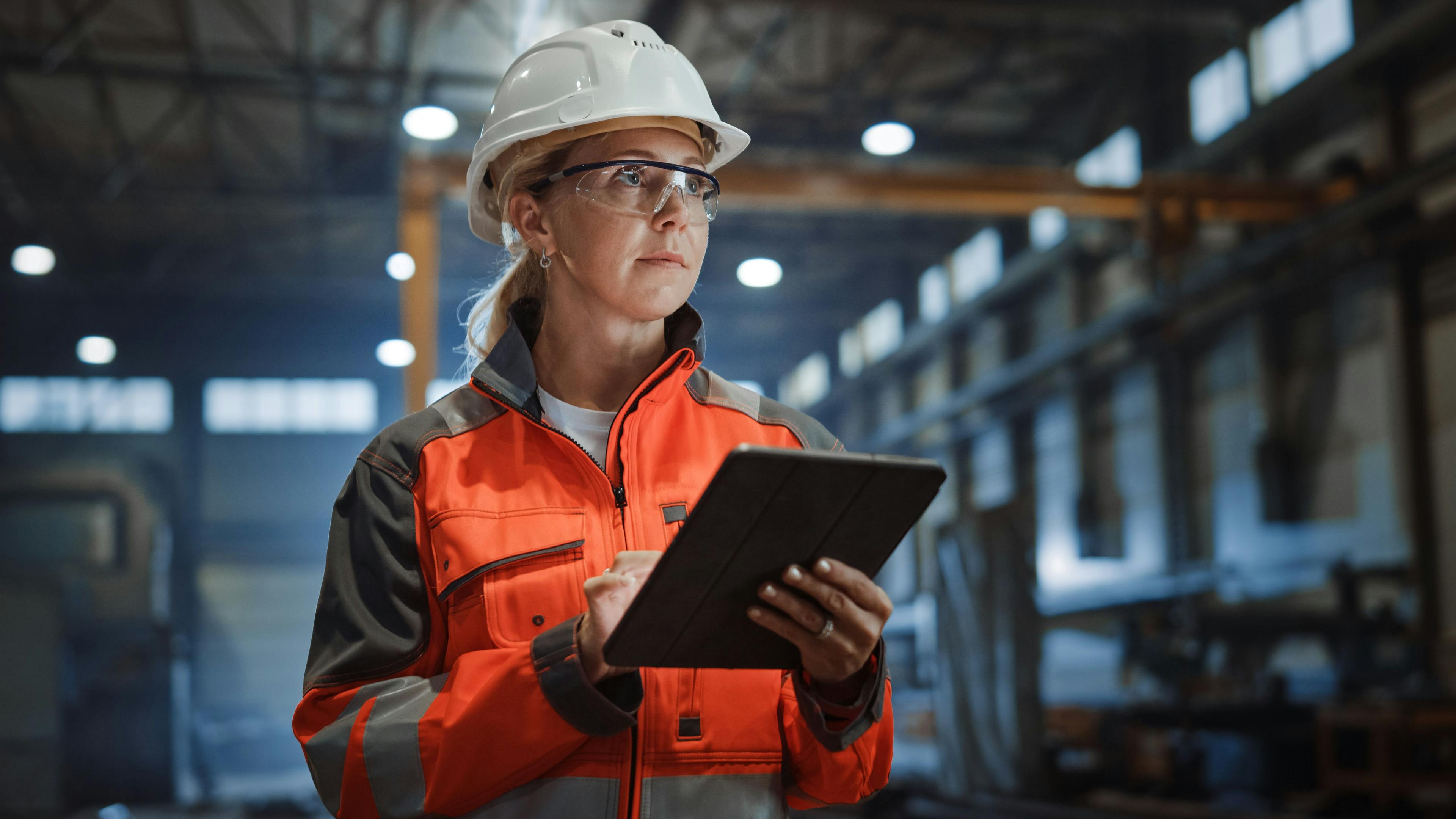 Professional Heavy Industry Engineer/Worker Wearing Safety Uniform and Hard Hat Uses Tablet Computer. Serious Successful Female Industrial Specialist Walking in a Metal Manufacture Warehouse. | Image Credit: © Gorodenkoff - stock.adobe.com