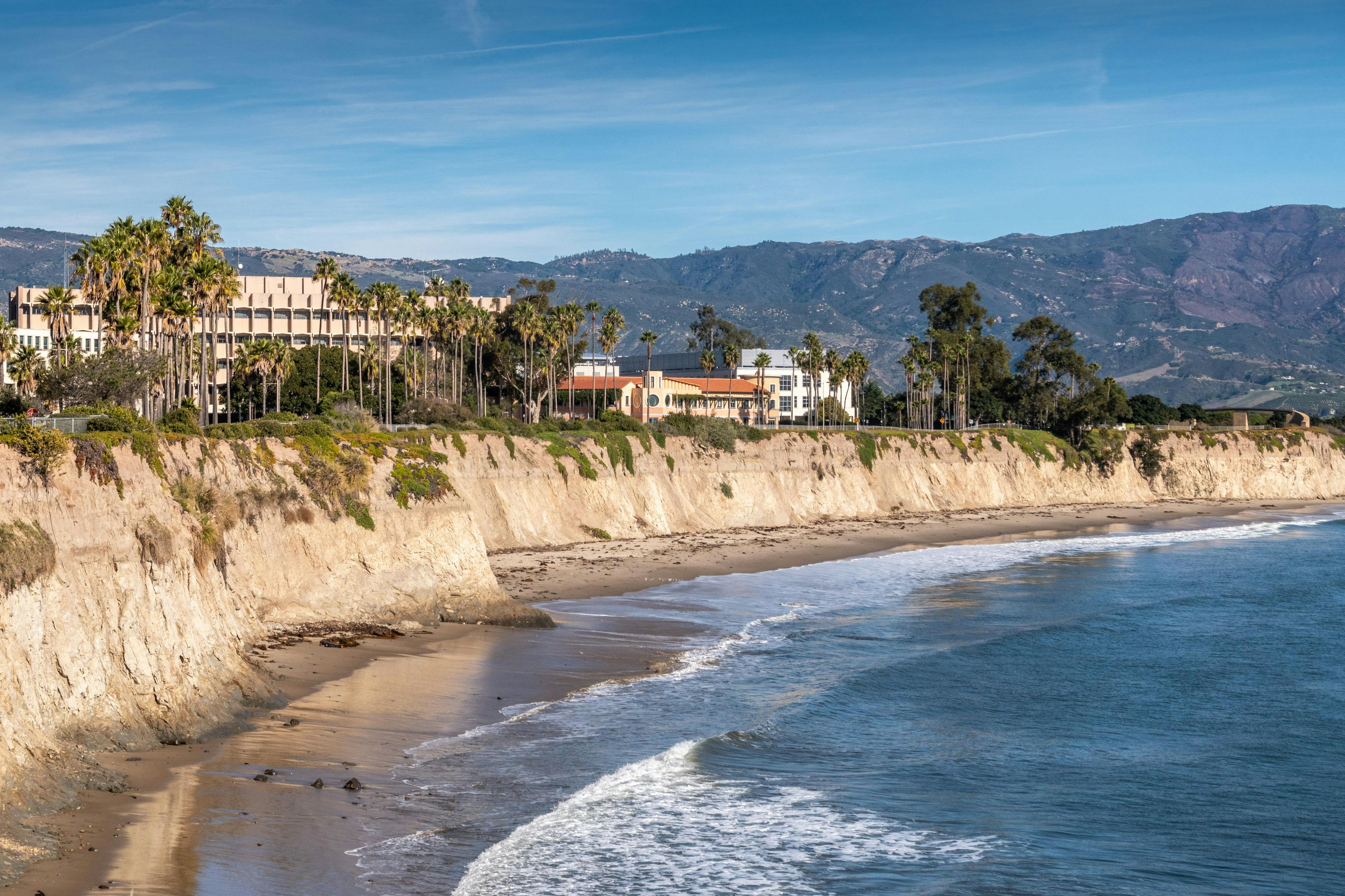 UCSB, University California Santa Barbara. East side beige cliffs in front of several buildings. Blue ocean in front. Green foliage around. Hills on horizon and blue | Image Credit: © Klodien – stock.adobe.com
