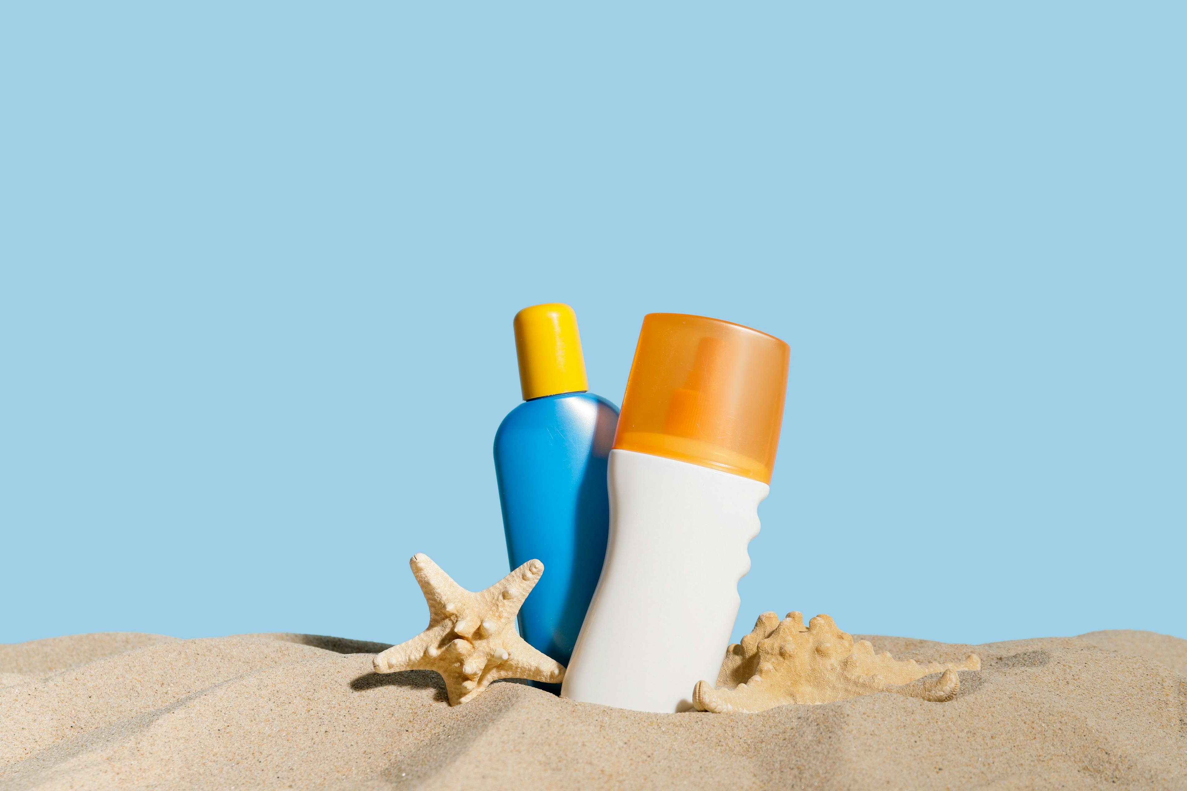 Bottles of sunscreen cream on sand against color background | Image Credit: © Pixel-Shot - stock.adobe.com 