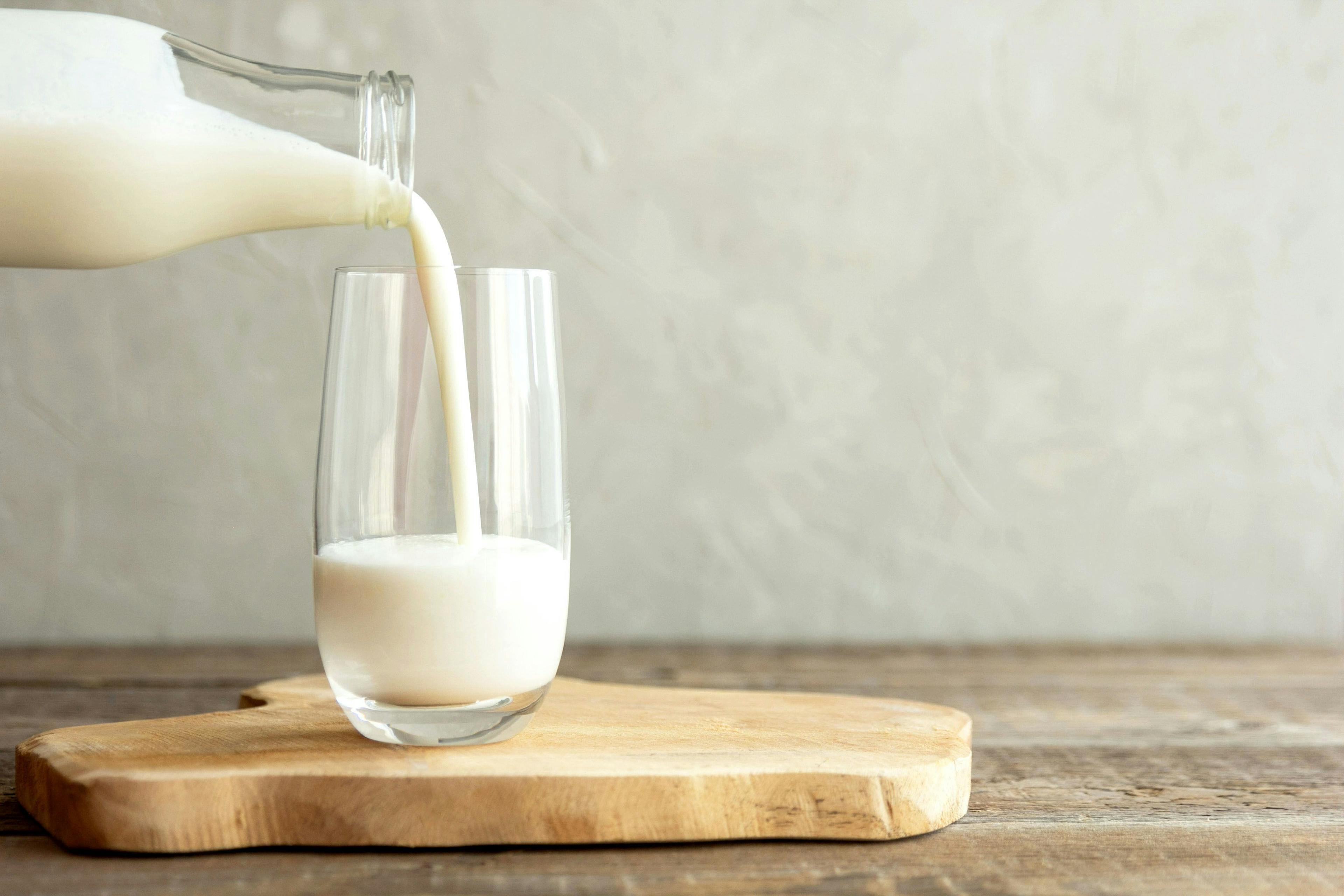 Kefir, milk or Turkish Ayran drink are poured into a glass cup from a bottle. A glass stands on a wooden stand on a rustic wooden table. | Image Credit: © Elena Medoks - stock.adobe.com