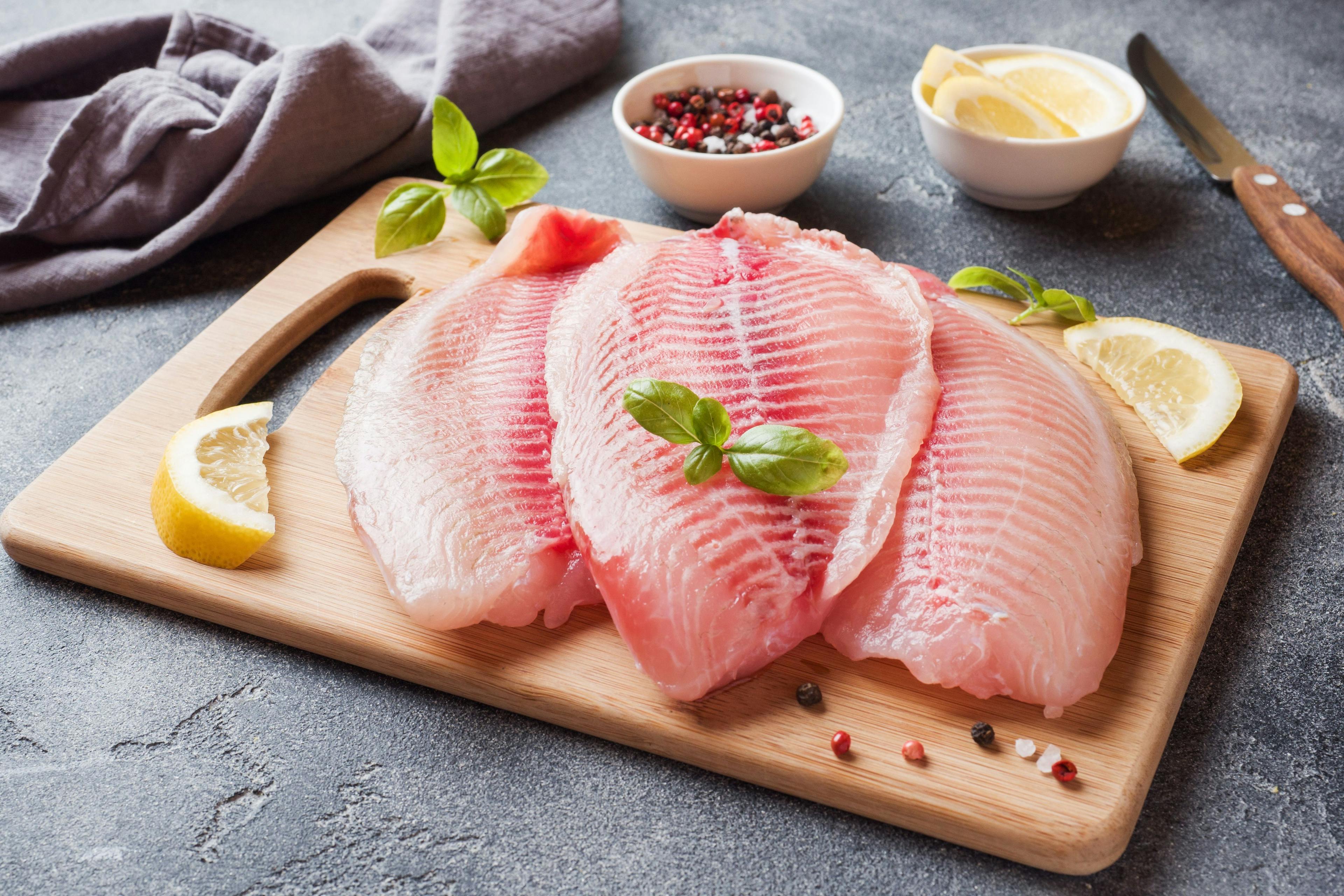 Raw fish fillet of tilapia on a cutting Board with lemon and spices. Dark table with copy space. | Image Credit: © Elenglush - stock.adobe.com 