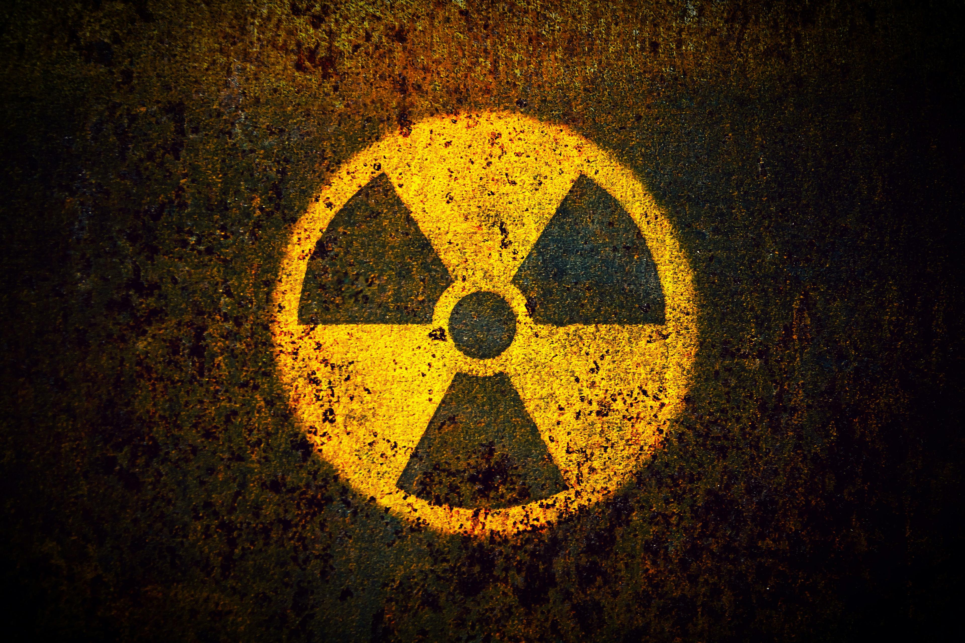 Round yellow radioactive (ionizing radiation) danger symbol painted on a massive rusty metal wall with dark rustic grungy texture background with vignetting. | Image Credit: © fewerton - stock.adobe.com