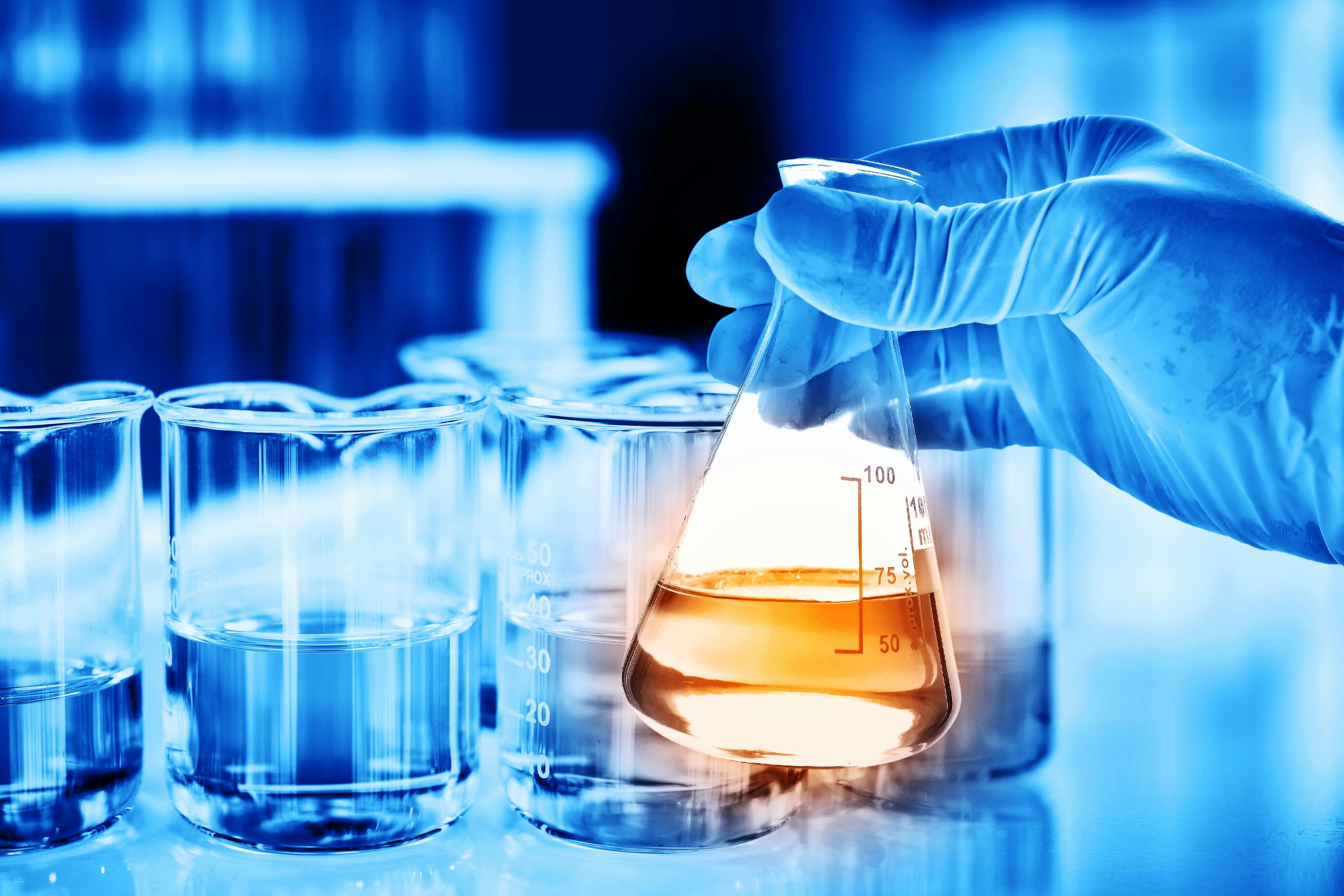 Flask in scientist hand with lab glassware background in laboratory. Science or chemical research and development concept. | Image Credit: © totojang1977 - stock.adobe.com.